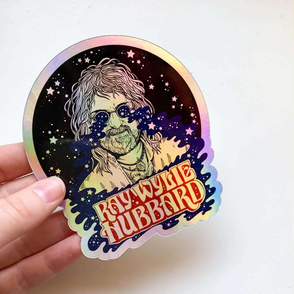 Holographic sticker with a stylized portrait and 'Kwylkee Hubbard' text, held by a hand on a white background.