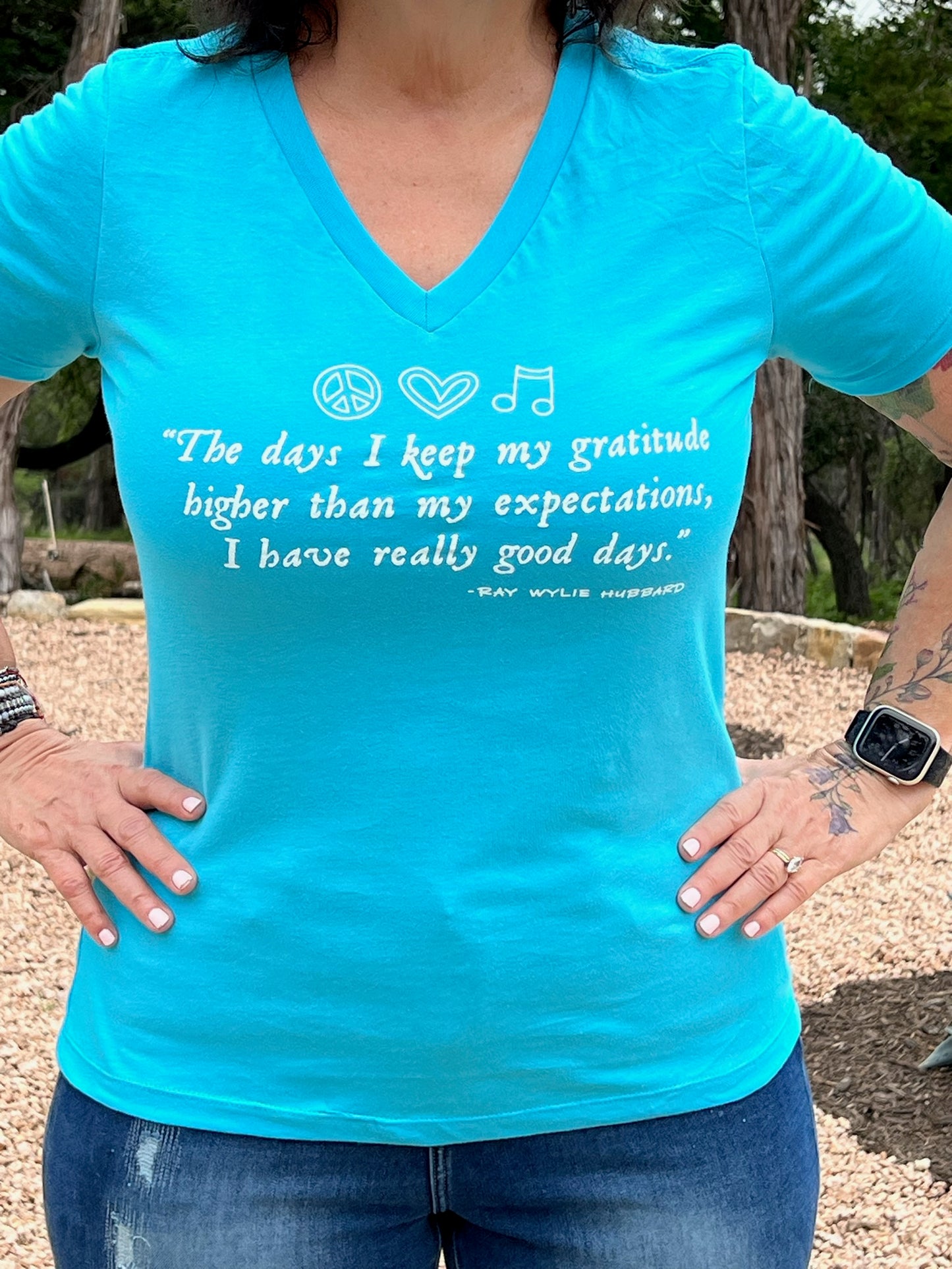 A woman wearing a blue V-neck t-shirt with a quote by Ray Wylie Hubbard printed on the front.